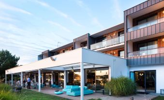 a modern building with a blue awning and patio furniture is surrounded by grass and trees at Best Western Plus Hotel les Rives du Ter