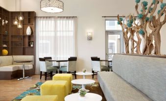 a modern living room with white walls , wooden floors , and large windows , featuring yellow and gray couches , white tables , and various decorative at Homewood Suites by Hilton Augusta, ME