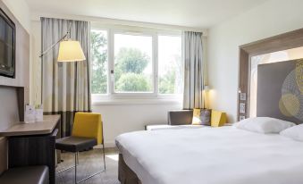 a hotel room with a large bed , two nightstands , and a window overlooking a park at Novotel le Mans