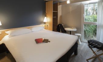 a hotel room with a large bed , a chair , and a desk with a laptop on it at Ibis Nantes Saint-Herblain