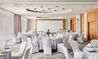 a large conference room with white chairs and tables , a screen , and multiple round tables at Sheraton Poznan Hotel