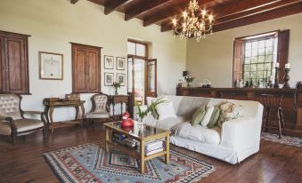 a spacious living room with wooden floors , white furniture , and a chandelier hanging from the ceiling at Schoone Oordt Country House