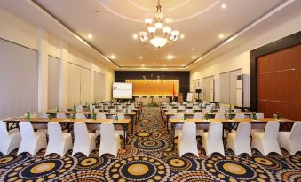 a large conference room with rows of tables and chairs , a projector screen at the front , and a chandelier hanging from the ceiling at Swiss-Belhotel Silae Palu