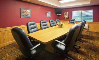 a conference room with a wooden table surrounded by black leather chairs and framed pictures on the wall at AmericInn by Wyndham Anamosa