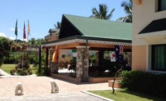 a resort with a green roof and flags , surrounded by palm trees and a parking lot at Hotel La Cretonne