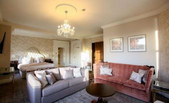 a living room with a pink couch , a gray couch , and a chandelier hanging from the ceiling at Makeney Hall Hotel