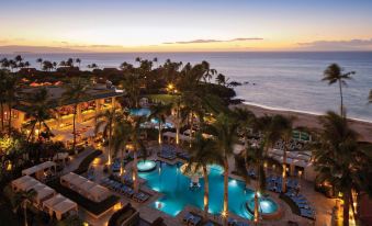 a resort with a large pool surrounded by palm trees and a beach in the background at Four Seasons Resort Maui at Wailea