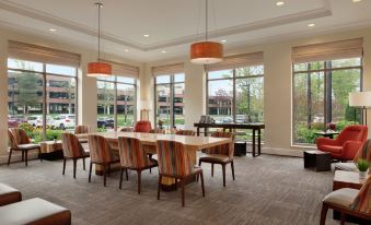a large dining room with a long table surrounded by chairs , and multiple windows providing natural light at Hilton Garden Inn Stony Brook