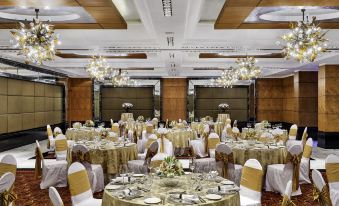 a large banquet hall with multiple round tables covered in gold tablecloths and chairs arranged for a formal event at Taj Club House