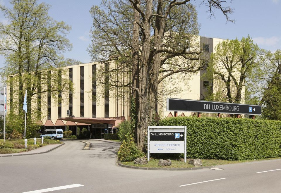 a large hotel building surrounded by trees , with a car parked in front of it at NH Luxembourg