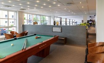 a pool table with a green felt surface is in the center of a room with a couch and windows at Pier 5 Hotel