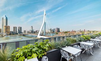 a rooftop patio with tables and chairs , overlooking a city skyline and a large white structure at Nhow Rotterdam
