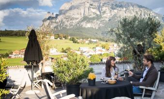 a woman sitting at a table on a balcony , enjoying a meal with a view of a mountainous landscape at Romantik Hotel Turm