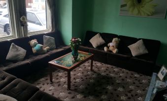 a living room with a black couch , wooden coffee table , and two teddy bears on the floor at Gracelands Guest House