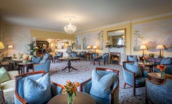 a well - decorated hotel lobby with a chandelier , paintings on the walls , and blue chairs and couches arranged around tables at The Inn at Dromoland