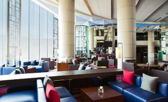 There is a restaurant located in the middle of the space, adjacent to an open living room area, featuring tables and chairs at Hong Kong SkyCity Marriott Hotel