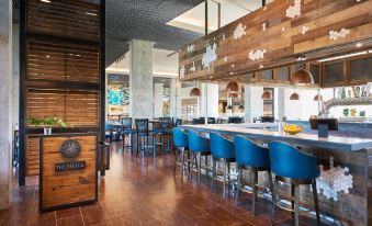a modern restaurant with wooden floors , blue chairs , and a long bar counter , decorated with christmas lights and ornaments at The Stella Hotel, Autograph Collection