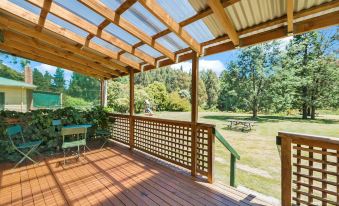 a wooden deck with a pergola and chairs , surrounded by green grass and trees , providing a serene outdoor setting at Giants Table and Cottages