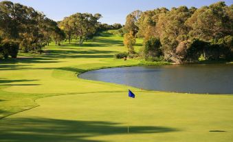 a golf course with green grass , trees , and water , as well as a blue flag in the foreground at Joondalup Resort