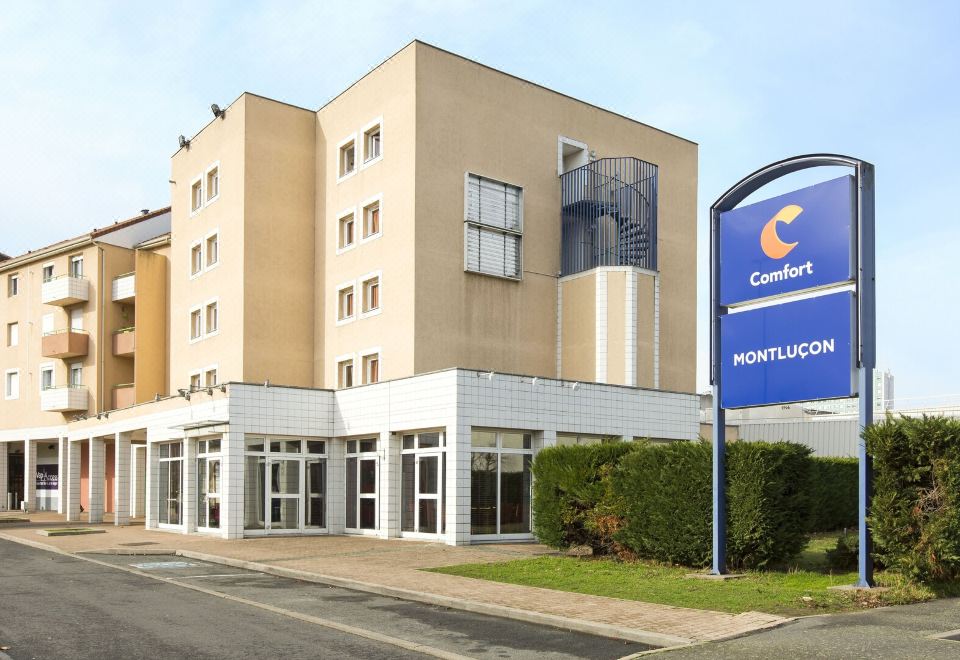 a large hotel building with a blue sign and a street in front of it at Comfort Hotel Montlucon