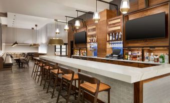 a modern bar area with a long white counter , wooden chairs , and various bottles and glasses on the counter at Doubletree by Hilton Columbus Dublin