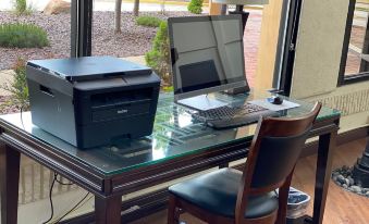 a desk with a computer , printer , and mouse is set up in front of a window at The Atrium Hotel on Third