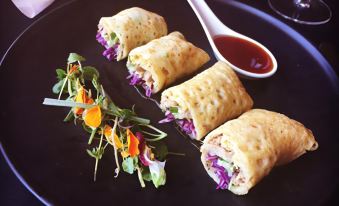 a plate with four egg rolls and a side salad , accompanied by a bowl of sauce at Emerald Explorers Inn