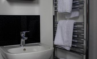 a white sink is next to a bathroom with towels on a rack and a black wall at Crofts Hotel
