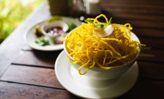 a white bowl filled with yellow noodles and a piece of lemon on top , placed on a wooden table at Our Jungle House