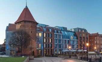 a red brick building with a tall spire , situated next to a body of water at Hilton Gdansk