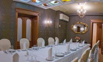 a long dining table is set with white plates , silverware , and wine glasses in a room with a chandelier and purple ceiling at Hotel Parus