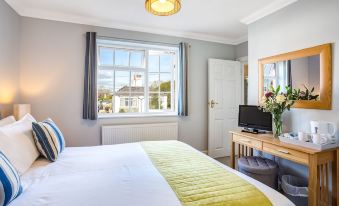 a well - lit hotel room with a bed , window , and window sill , decorated with flowers and a tv at The Coast House B&B