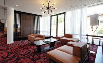 a modern living room with red carpeting , large windows , and brown leather couches arranged around a coffee table at Hampton by Hilton Toulouse Airport