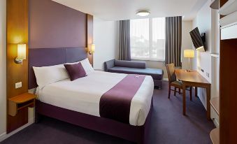 a large bed with a purple headboard and white sheets is in the center of a hotel room at Premier Inn Dover East