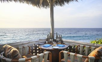 a beachside dining area with a table set for a meal , surrounded by chairs and overlooking the ocean at JW Marriott Maldives Resort & Spa