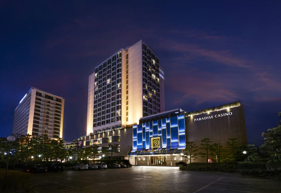a large , modern hotel building with a lit - up sign and a parking lot in front of it at Paradise Hotel Busan