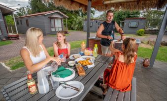 a family of four is gathered around a picnic table , enjoying a meal and each other 's company at Adelaide Caravan Park - Aspen Holiday Parks