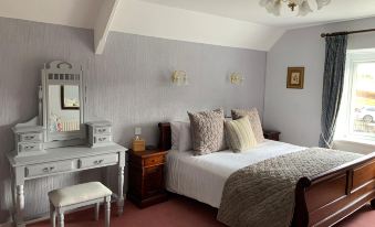a cozy bedroom with a white bed , a dresser , and a mirror , as well as a chair and a table in the room at Lydgate House Hotel