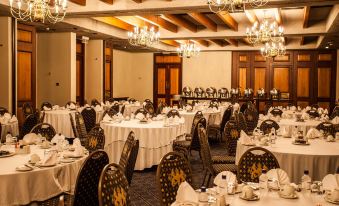 a large dining room with multiple tables covered in white tablecloths and chairs arranged for a formal event at The Royal Hotel by Coastlands Hotels & Resorts