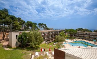 a beautiful hotel with a swimming pool , surrounded by trees and grass , under a blue sky with clouds at Aparthotel Comtat Sant Jordi