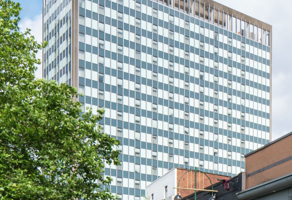 a tall , white and blue striped building with a red sign on the top is surrounded by trees at Hampton by Hilton Birmingham Broad Street