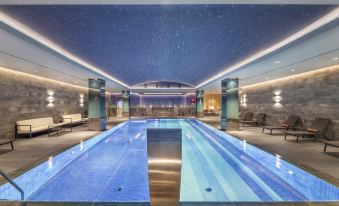 an indoor swimming pool surrounded by lounge chairs , where people are relaxing and enjoying their time at DoubleTree by Hilton Skopje