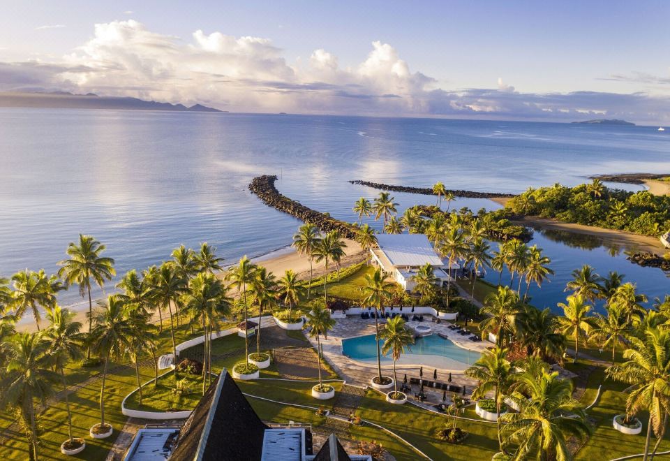 a bird 's eye view of a resort with palm trees , a pool , and the ocean at The Pearl South Pacific Resort