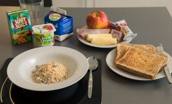 a table with a bowl of cereal , two plates of toast , an apple , yogurt , butter , and an apple at Quest Highbrook