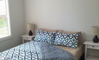 a neatly made bed with a blue and white patterned comforter , two lamps on either side of it , and a window in the background at Brighton Beachfront Holiday Park Adelaide