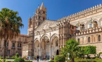 a large , ornate cathedral with a tall spire and people walking around it in the courtyard at Hotel Punta Nord Est