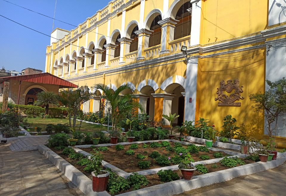 a yellow building with arches and a sign , surrounded by a courtyard filled with potted plants at Hotel Samrat