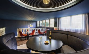 a modern restaurant with a black and blue color scheme , featuring a round dining table surrounded by couches at Mercure Versailles Paris Ouest