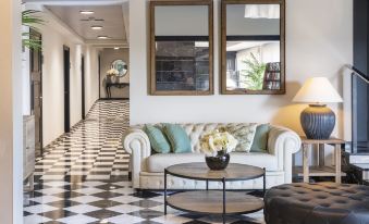 a white couch is sitting in a room with black and white checkered floor , next to two large mirrors at Salles Hotel Aeroport de Girona