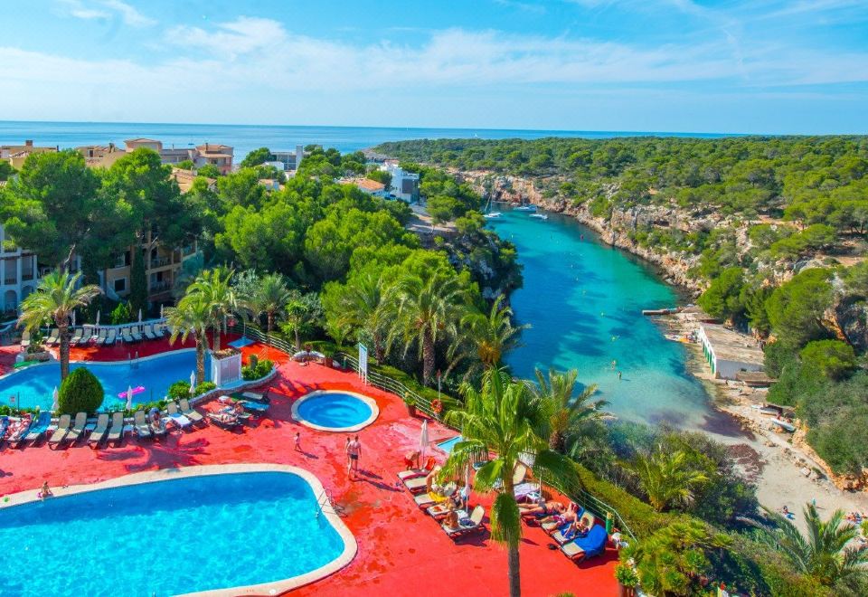 a beautiful resort with a large pool surrounded by palm trees and a river , creating a serene and inviting atmosphere at Aparthotel Ona Cala Pi Club